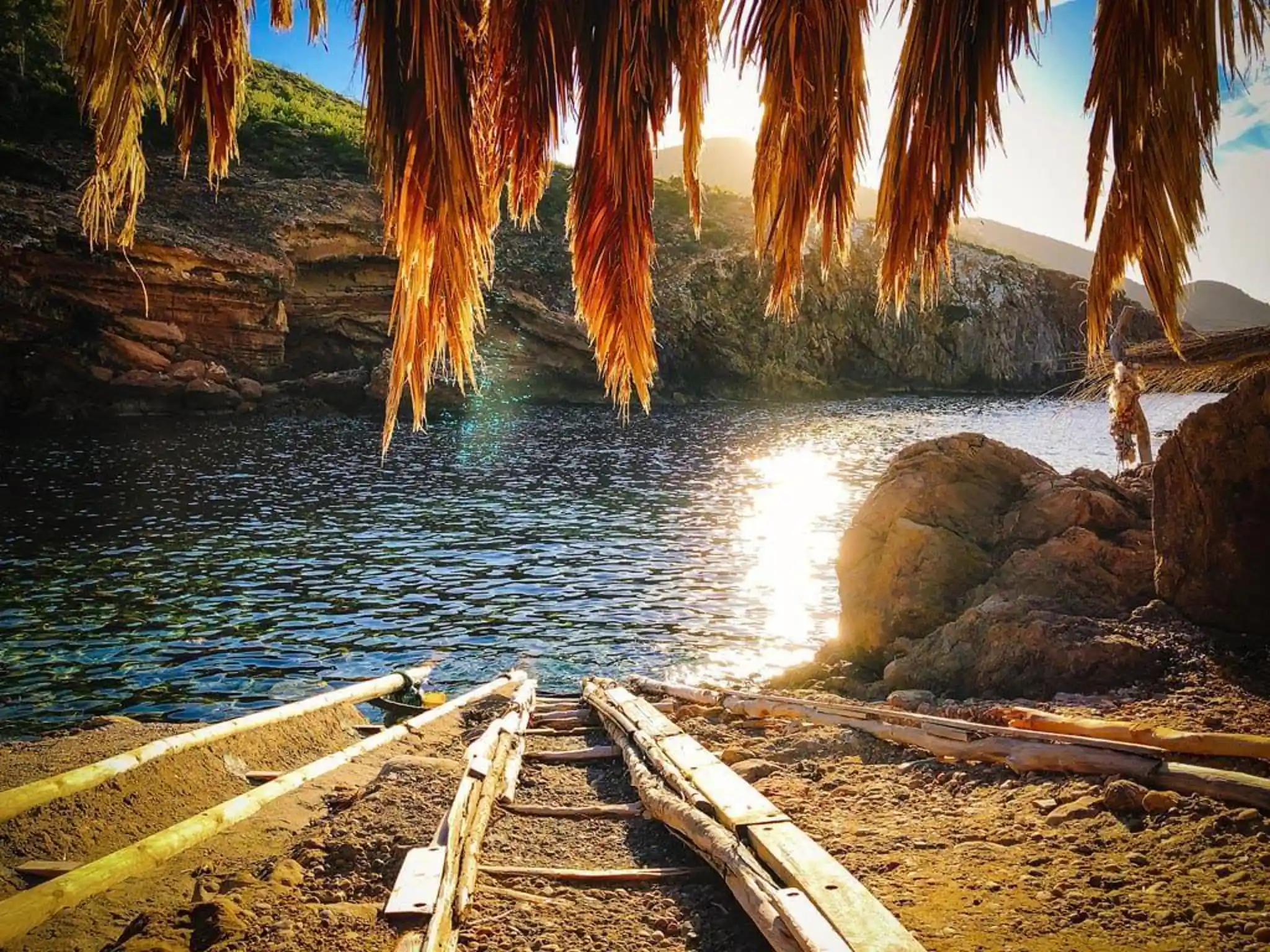Secluded Ibiza cove at sunset beneath palm leaves